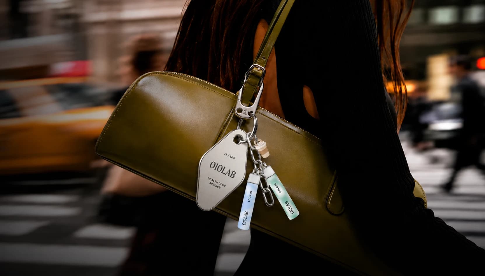 010LAB health-club keychain tag and cartridge charms clipped to a shoulder bag on a city street